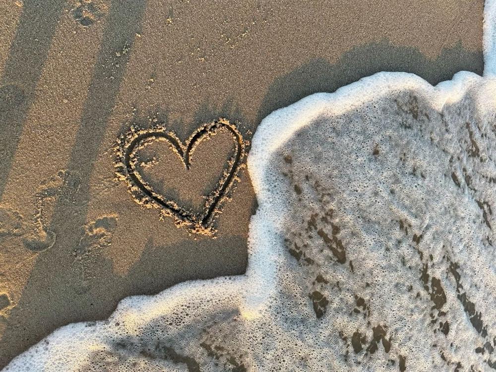 Corazón dibujado en la arena de la playa junto a la espuma del mar